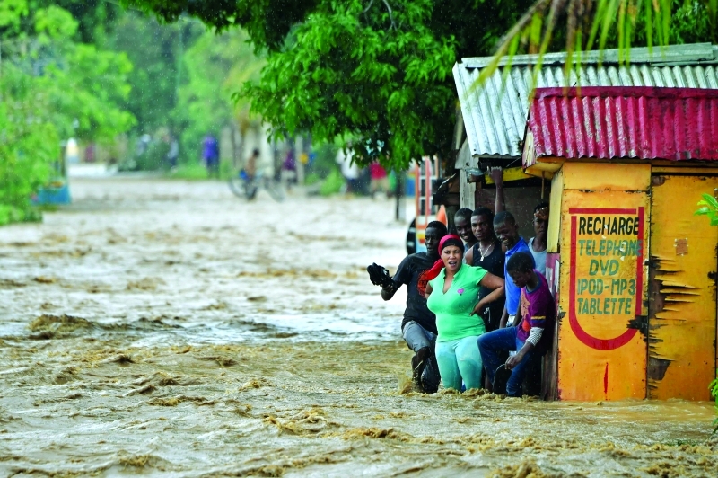 الصورة : TOPSHOT - People try to cross the overflowing La Rouyonne river in the commune of Leogane, south of Port-au-Prince, October 5, 2016. Haiti and the eastern tip of Cuba -- blasted by Matthew on October 4, 2016 -- began the messy and probably grim task of assessing the storm's toll. Matthew hit them as a Category Four hurricane but has since been downgraded to three, on a scale of five, by the US National Hurricane Center. / AFP / HECTOR RETAMAL