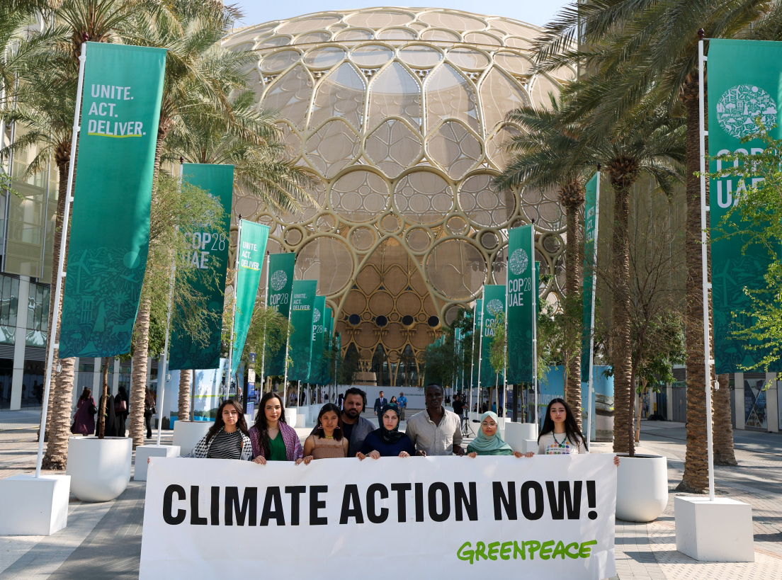 الصورة : نشطاء منظمة «السلام الأخضر» يحملون لافتة خلال مؤتمر الأطراف لتغيّر المناخ «كوب 28» في دبي | تصوير: دينيس مالاري